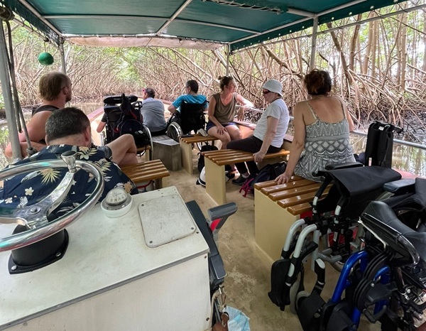Intérieur du bateau en pleine visite avec deux personnes à mobilité réduites dans leurs fauteuil à l'avant et deux fauteuils pliés à l'arrière.